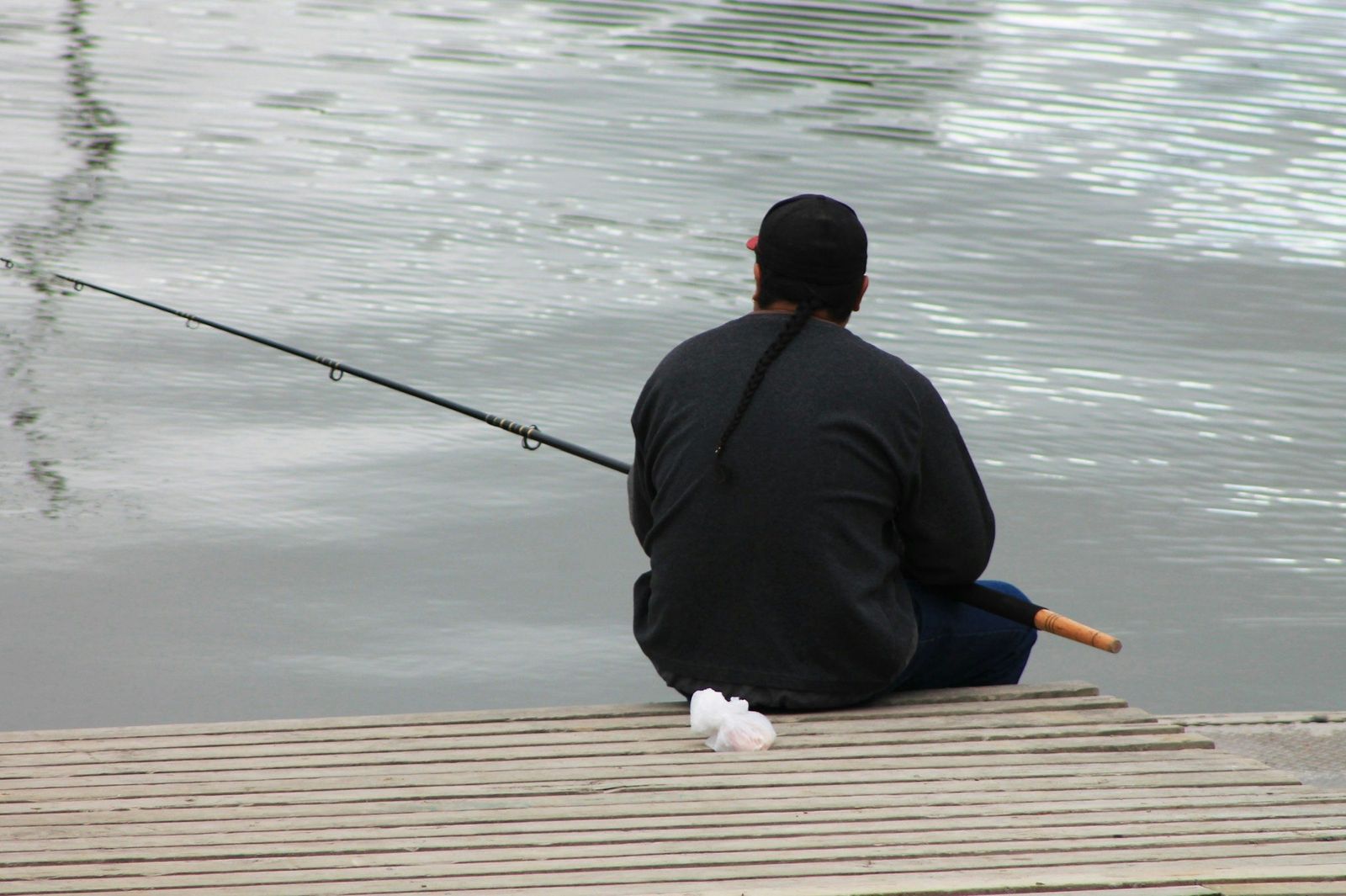 An angler fishing from a jetty at Whanganui with a bag of bait beside him