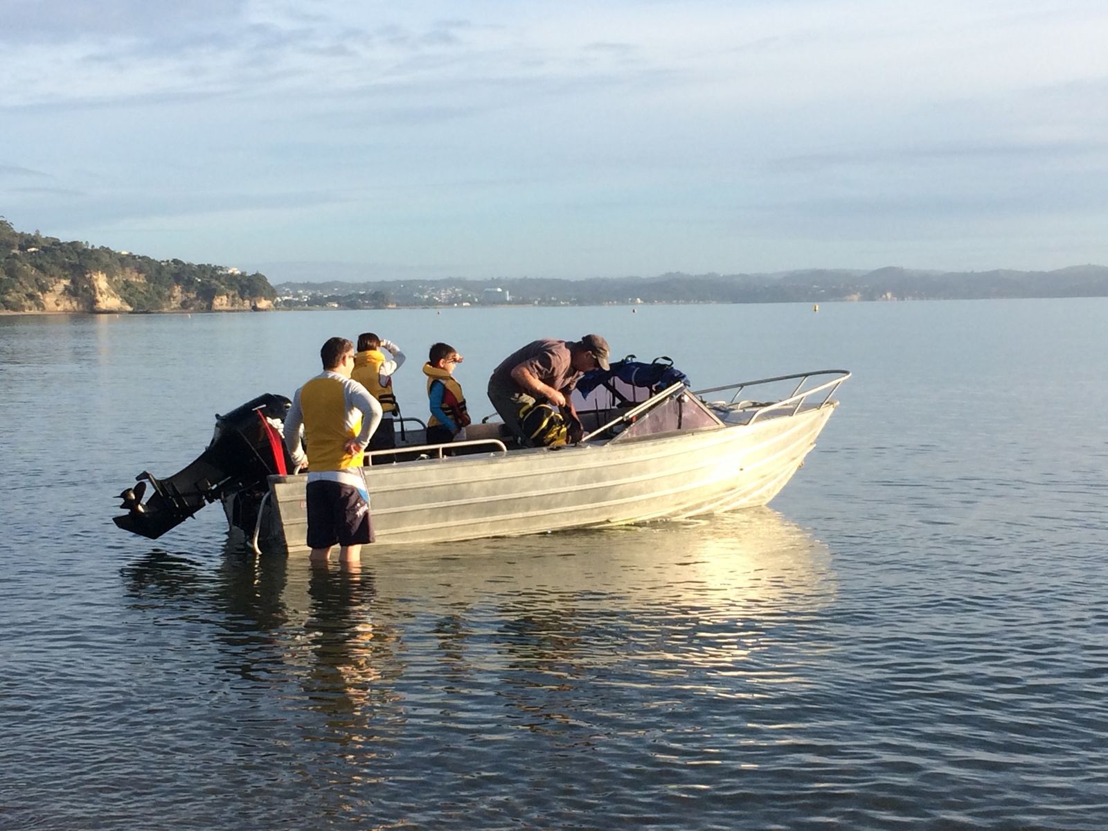 A family getting an aluminium runabout ready in the shallows at Stanmore Bay, the children in lifejackets