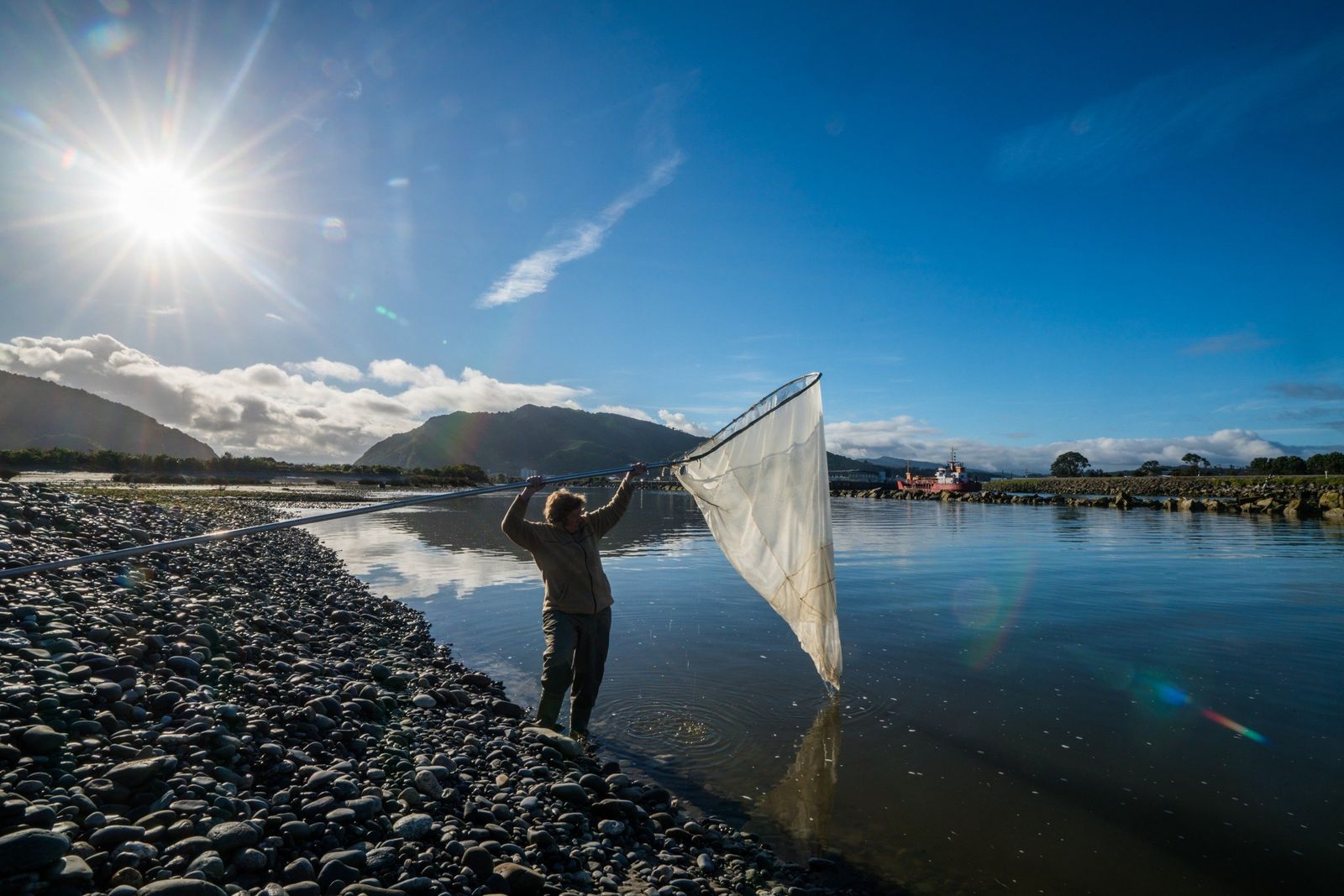 A whitebaiter with a scoop net on the river bank at Ōkārito